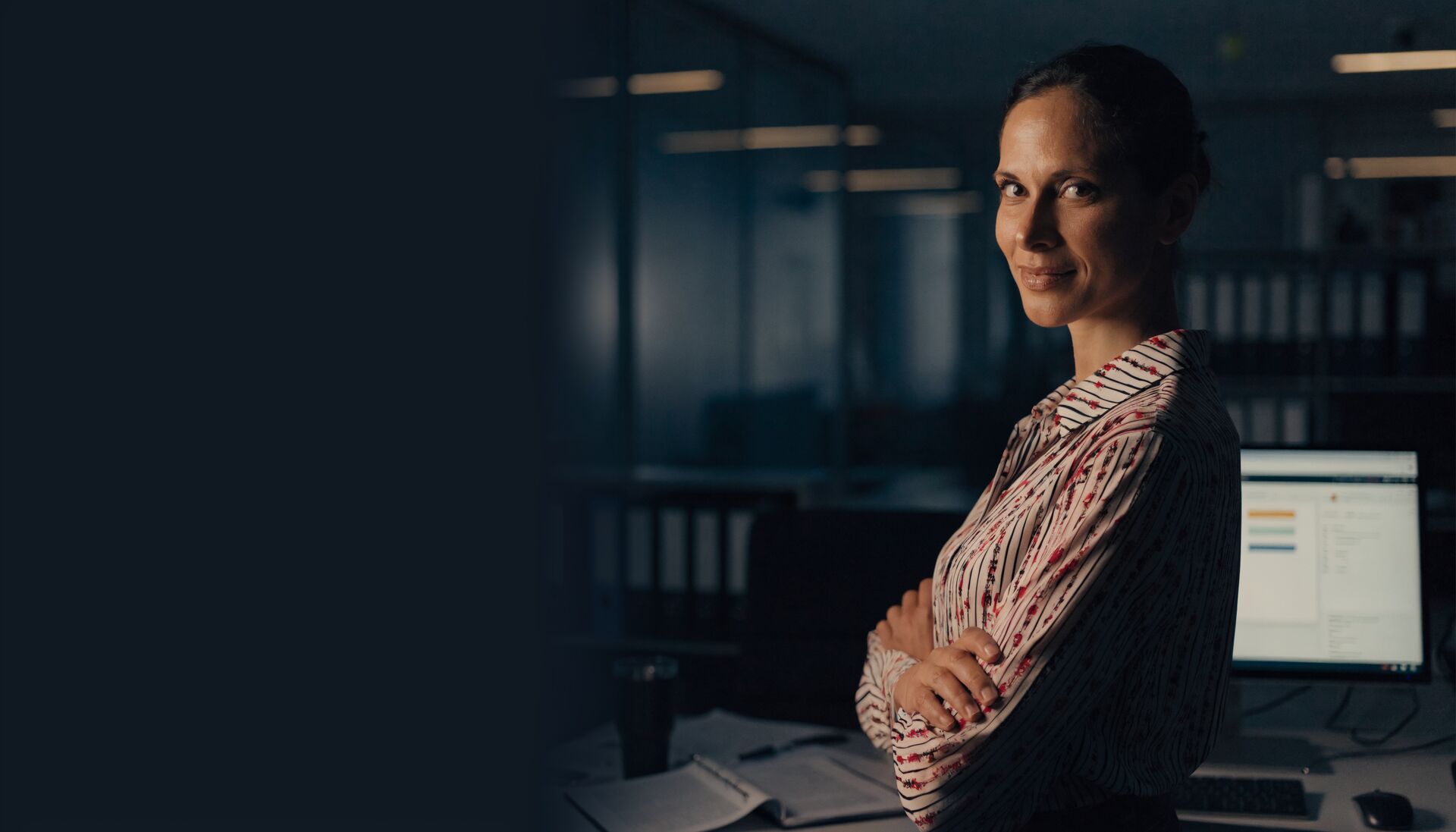 A sales rep with arms folded, quietly pleased, her desk and monitor behind her